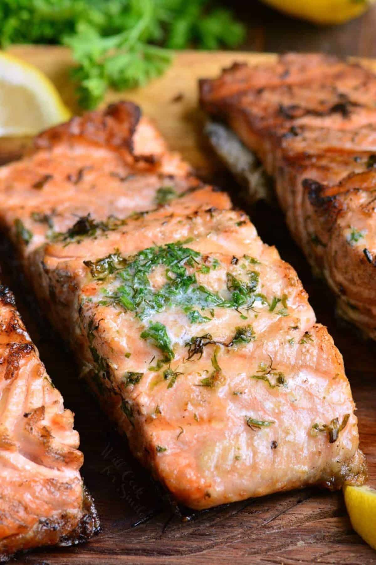 grilled salmon filet topped with herb butter melting off next to two other filets.