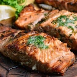 two grilled salmon filets on the wooden plate topped with melted herb butter.