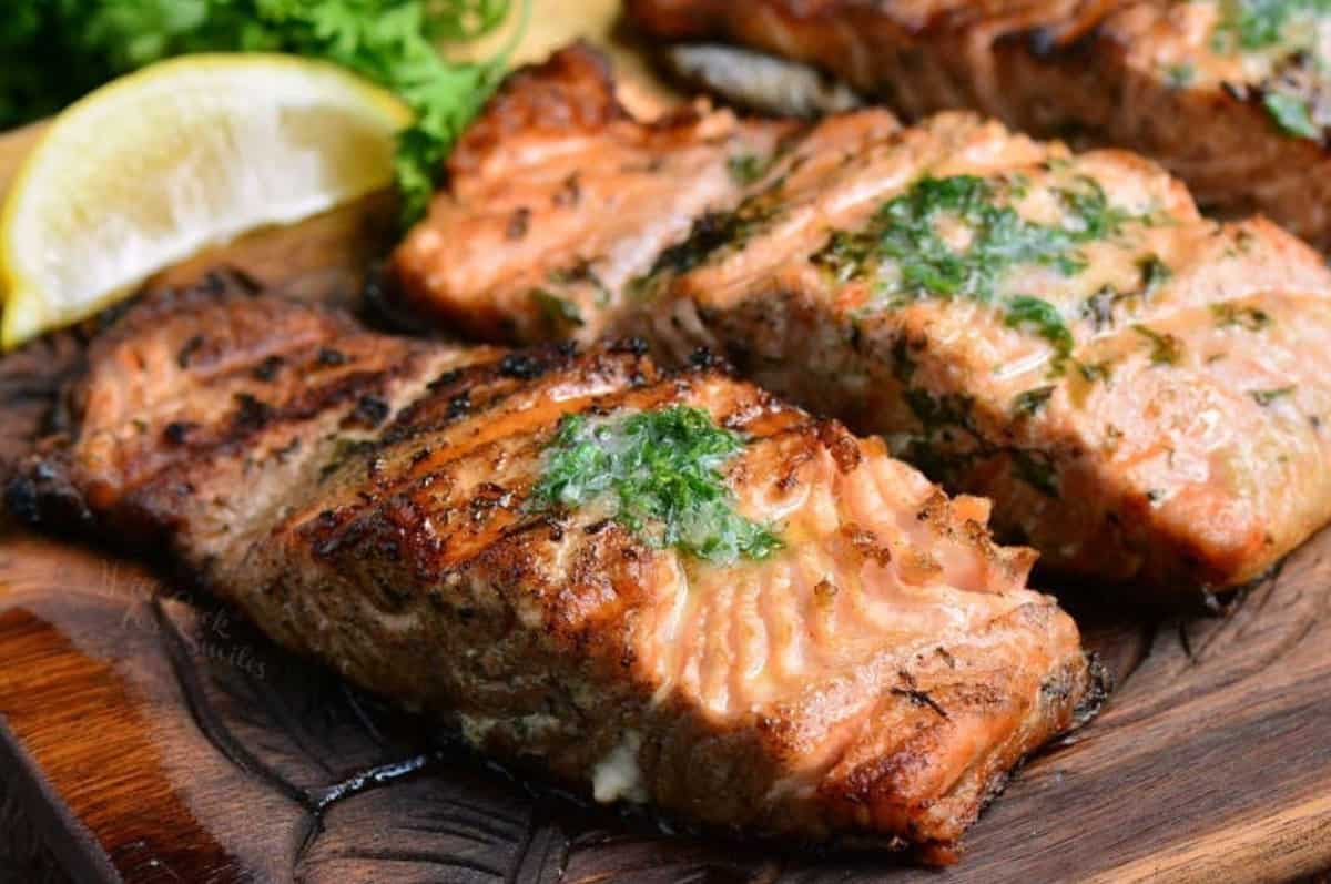 two grilled salmon filets on the wooden plate topped with melted herb butter.