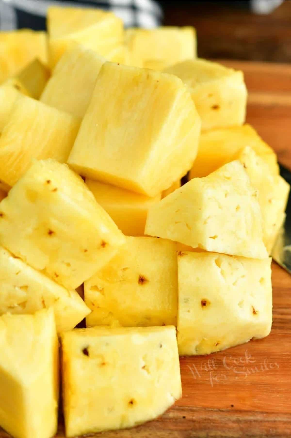 cup fresh pineapple chunks on a cutting board with part of a knife visible.
