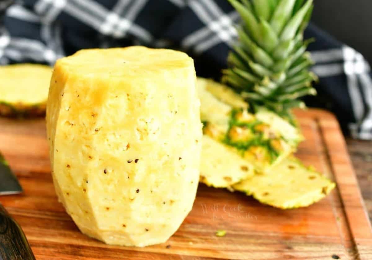 pineapple without the top, bottom, and skin on the cutting board with cut-off pieces behind.