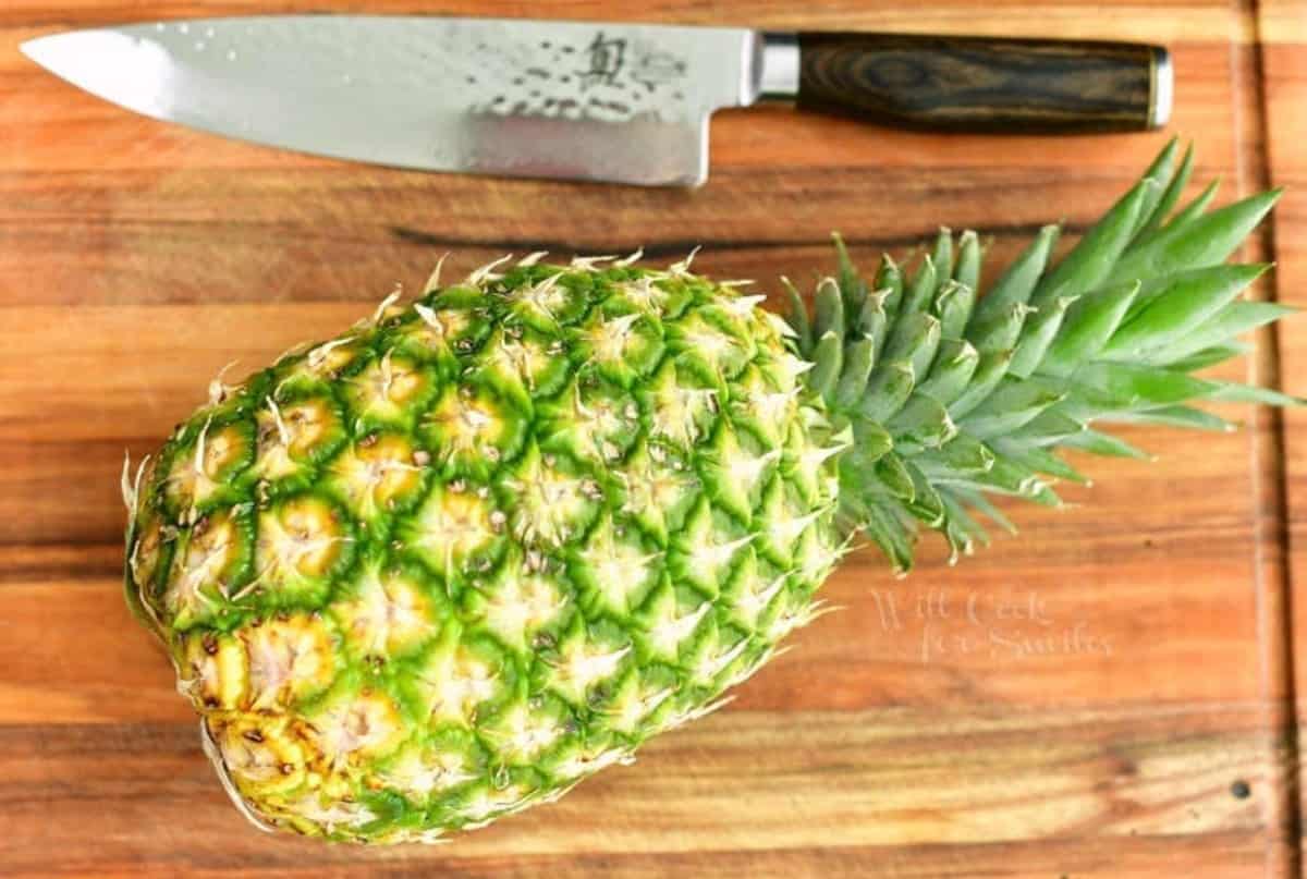 whole pineapple on a wooden cutting board with a knife next to it.