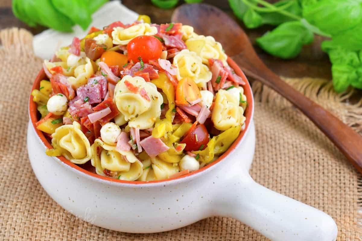 a light ceramic bowl filled with Italian tortellini salad and a wooden spoon next to it.