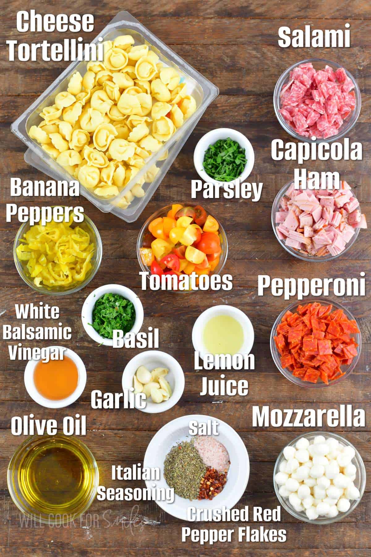 labeled ingredients to make Italian tortellini salad on a wooden board.