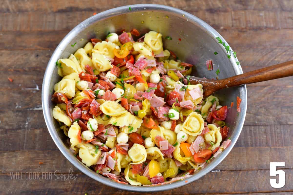 mixed Italian tortellini salad in a metal mixing bowl with a wooden spoon.