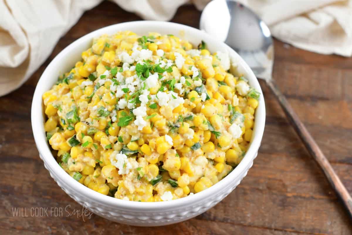Mexican street corn salad in a white bowl with a spoon next to it.