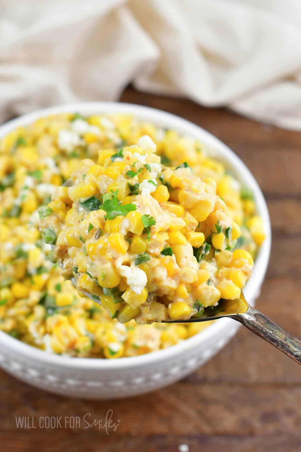 scooping out some creamy Mexican street corn salad with a large spoon.