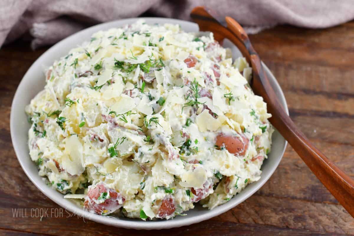 creamy herb and parmesan potato salad in a gray bowl with a wooden spoon.