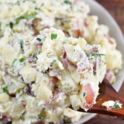 some creamy potato salad scooped on the wooden spoon next to the bowl.