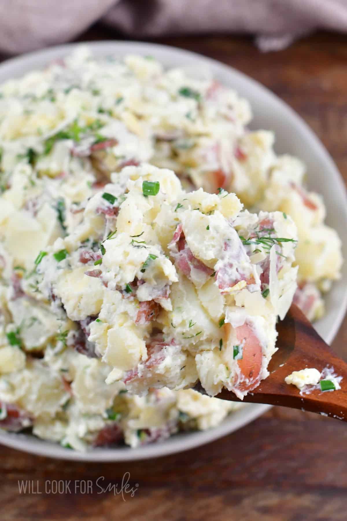 some creamy potato salad scooped on the wooden spoon next to the bowl.