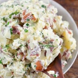 scooping some parmesan herb potato salad with a wooden spoon.