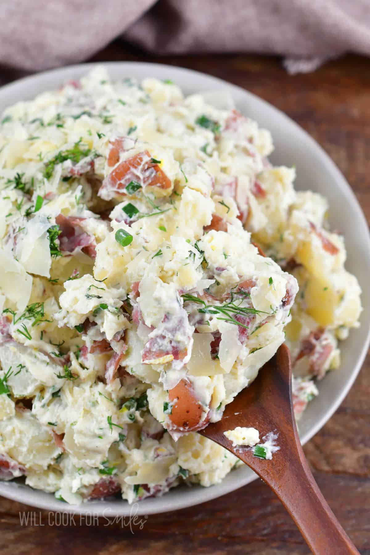 scooping some parmesan herb potato salad with a wooden spoon.