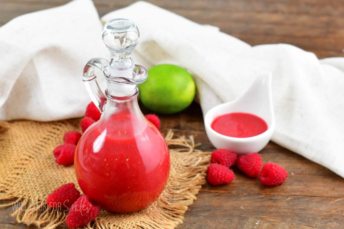 bright pink raspberry vinaigrette in glass jar with berries and lime around.