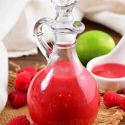 tall glass dressing jar with bright raspberry vinaigrette in it and berries around.