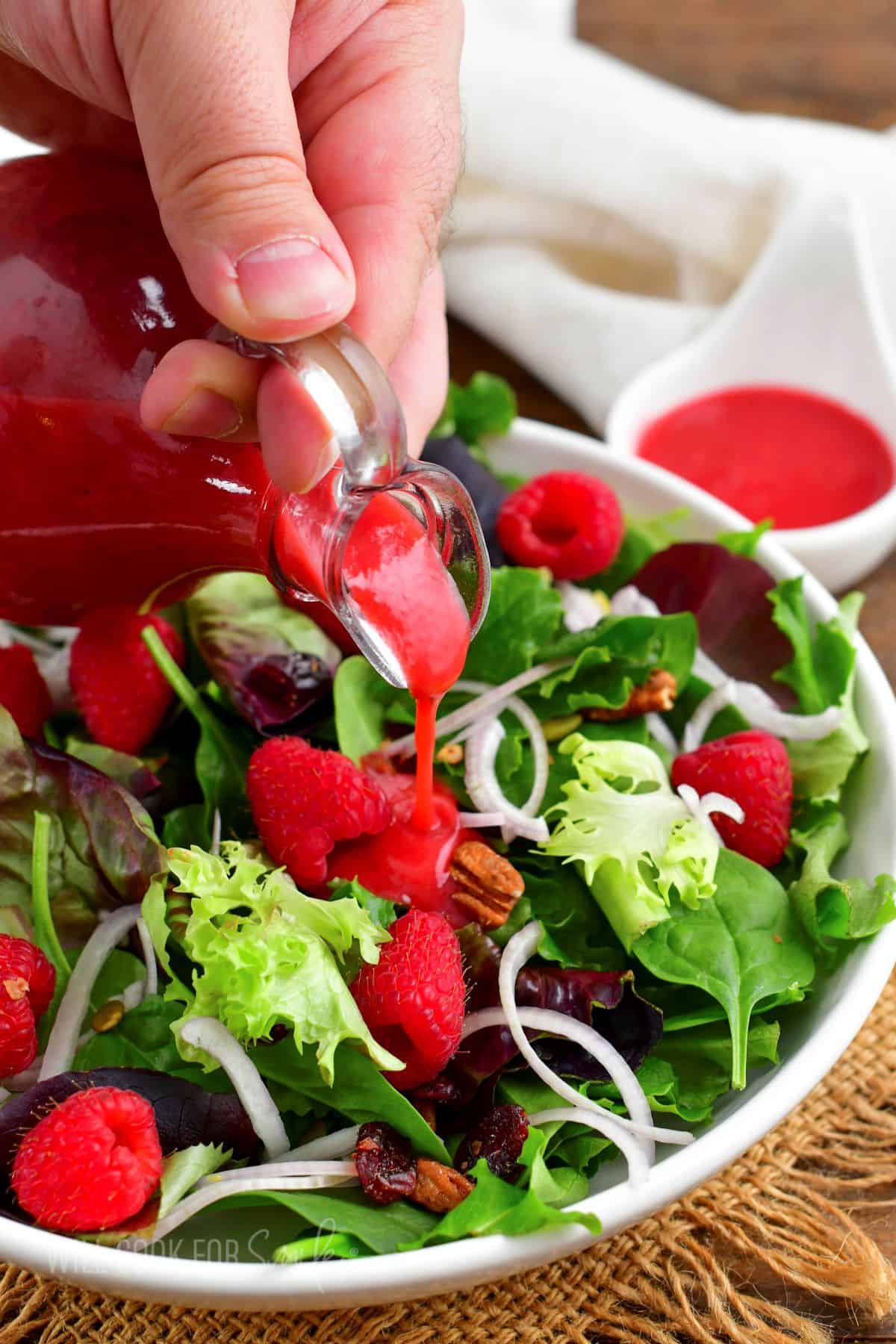 pouring raspberry vinaigrette over a bright salad with berries and nuts.
