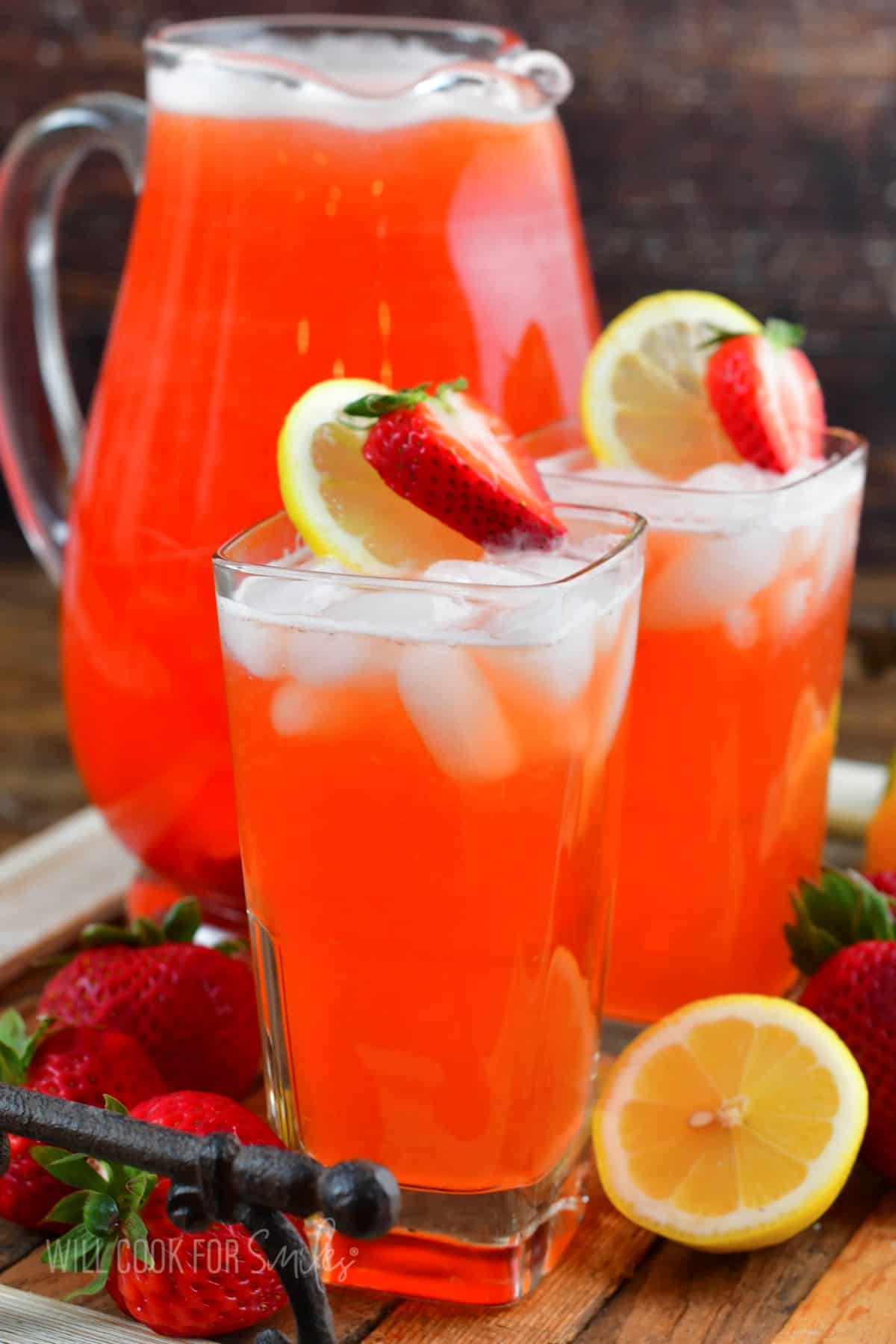 two glasses filled with strawberry lemonade next to a pitcher filled as well.