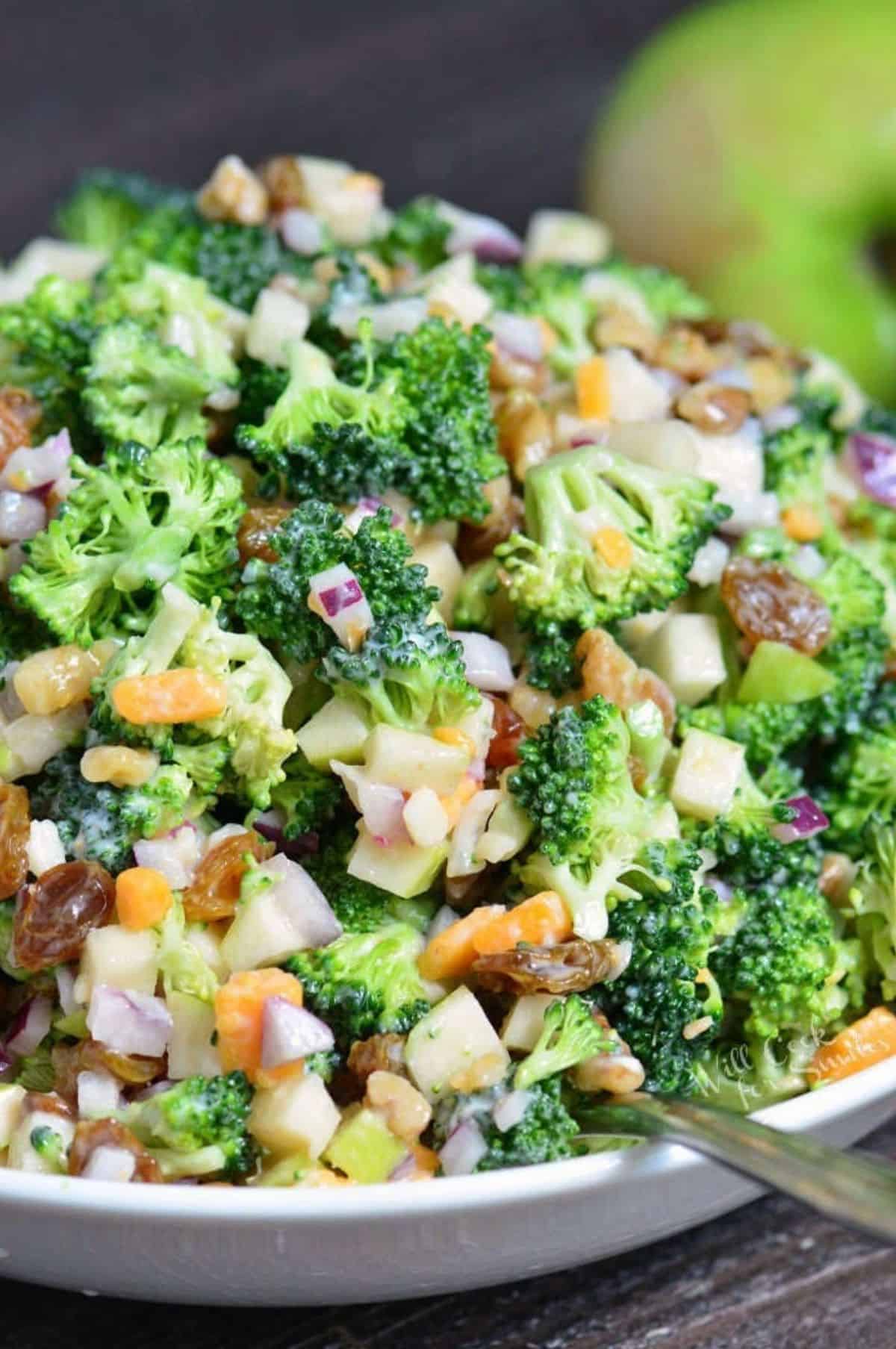 A tossed broccoli salad is presented in a white bowl. 