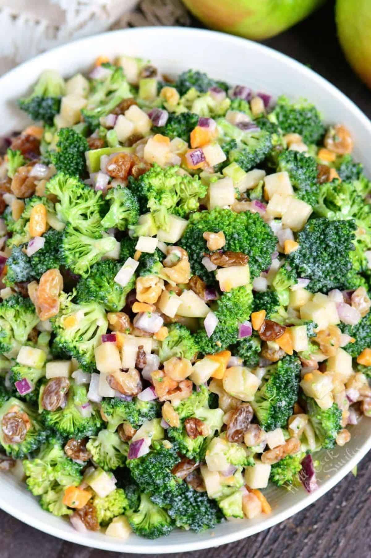 broccoli salad with apples, nuts, and cheese mixed with creamy dressing in a bowl.