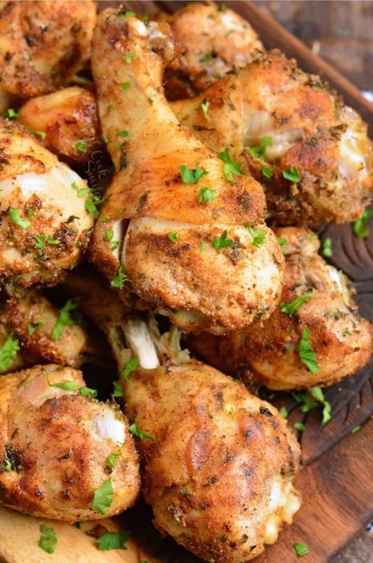 A batch of baked chicken drumsticks is garnished with fresh parsley. 