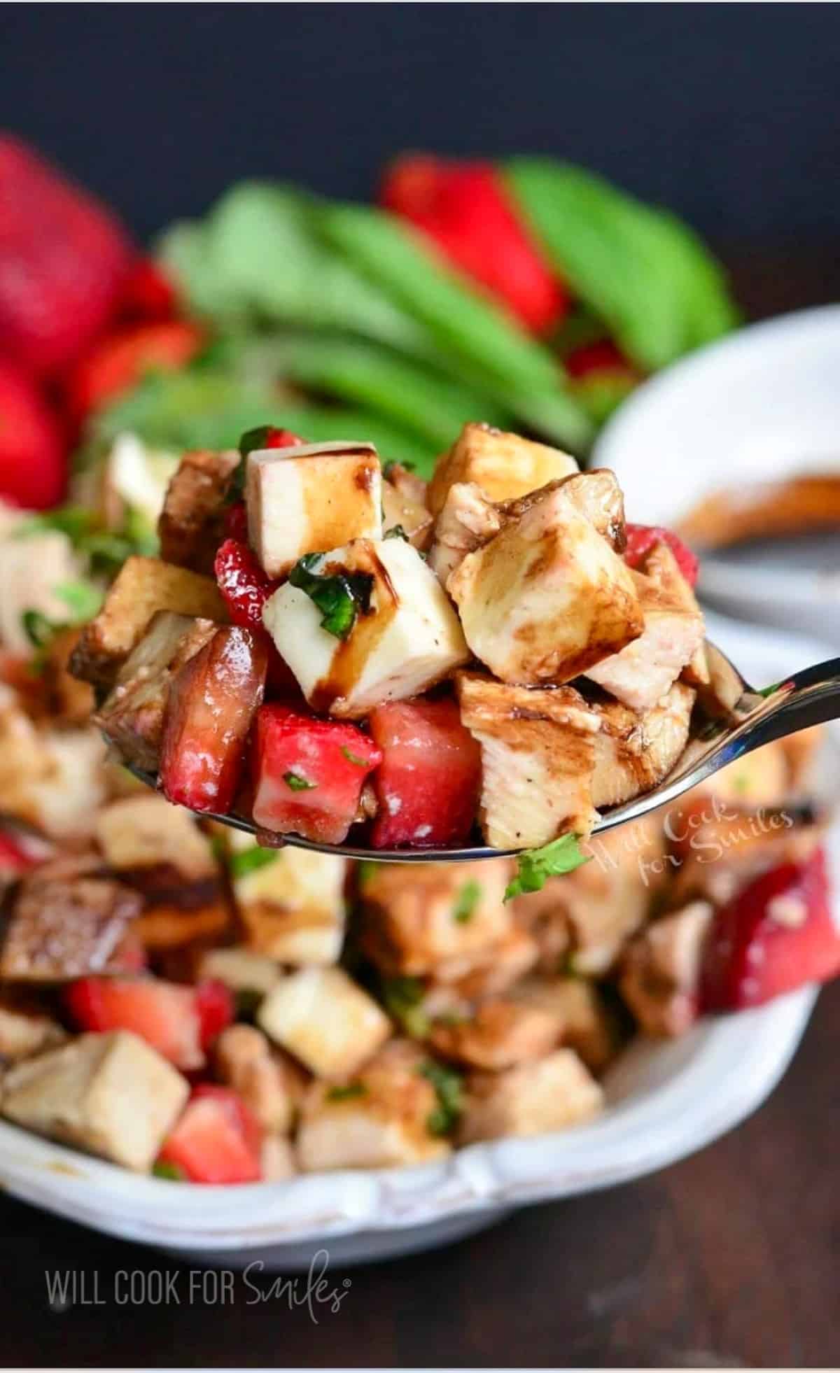 A spoon is lifting a portion of chicken salad above the bowl. 