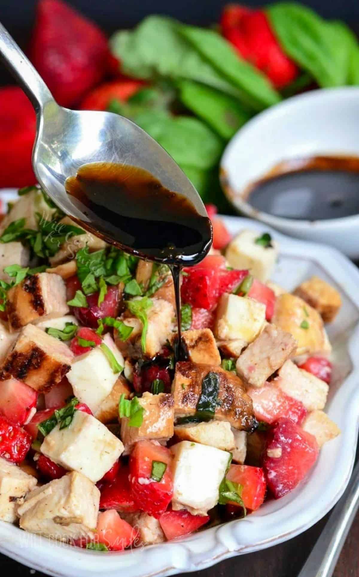 Balsamic reduction is being poured on top of a chicken strawberry salad.
