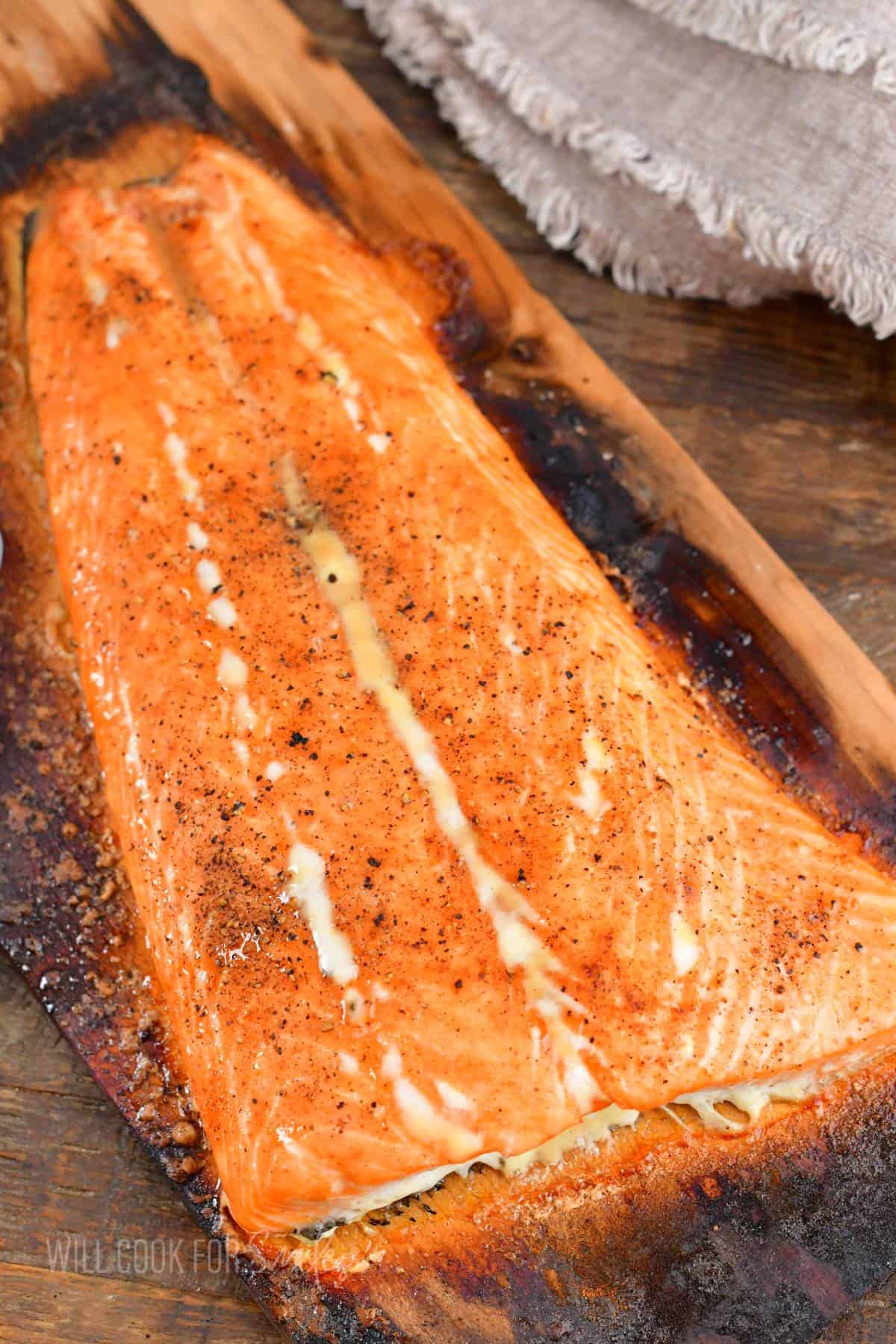 A whole salmon filet is fully cooked on a cedar plank. 