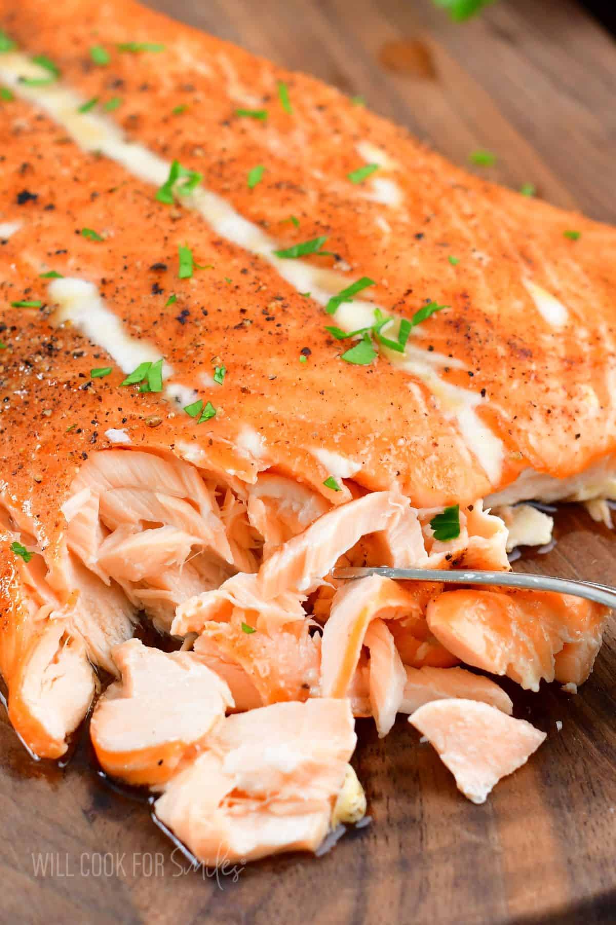 A large, cooked whole salmon filet is being flaked with a fork. 