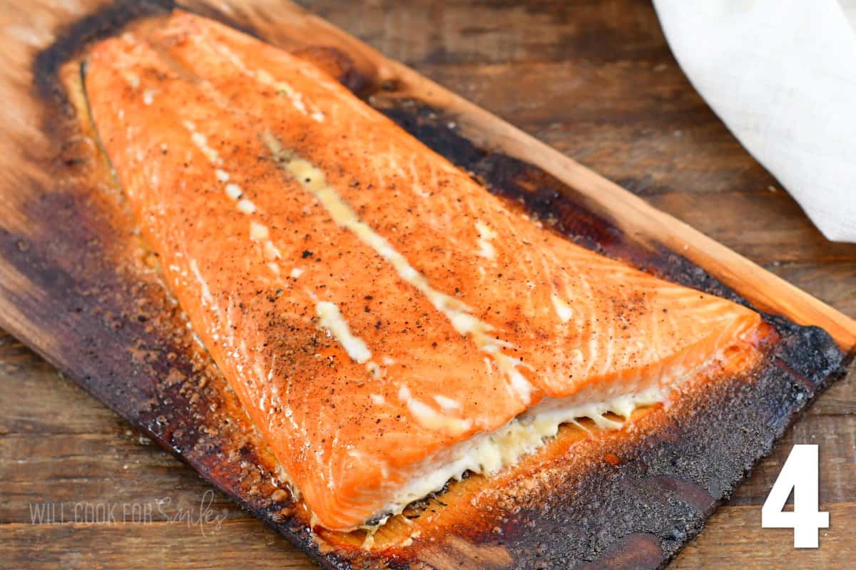 Cooked salmon is presented on a lightly charred wood plank. 