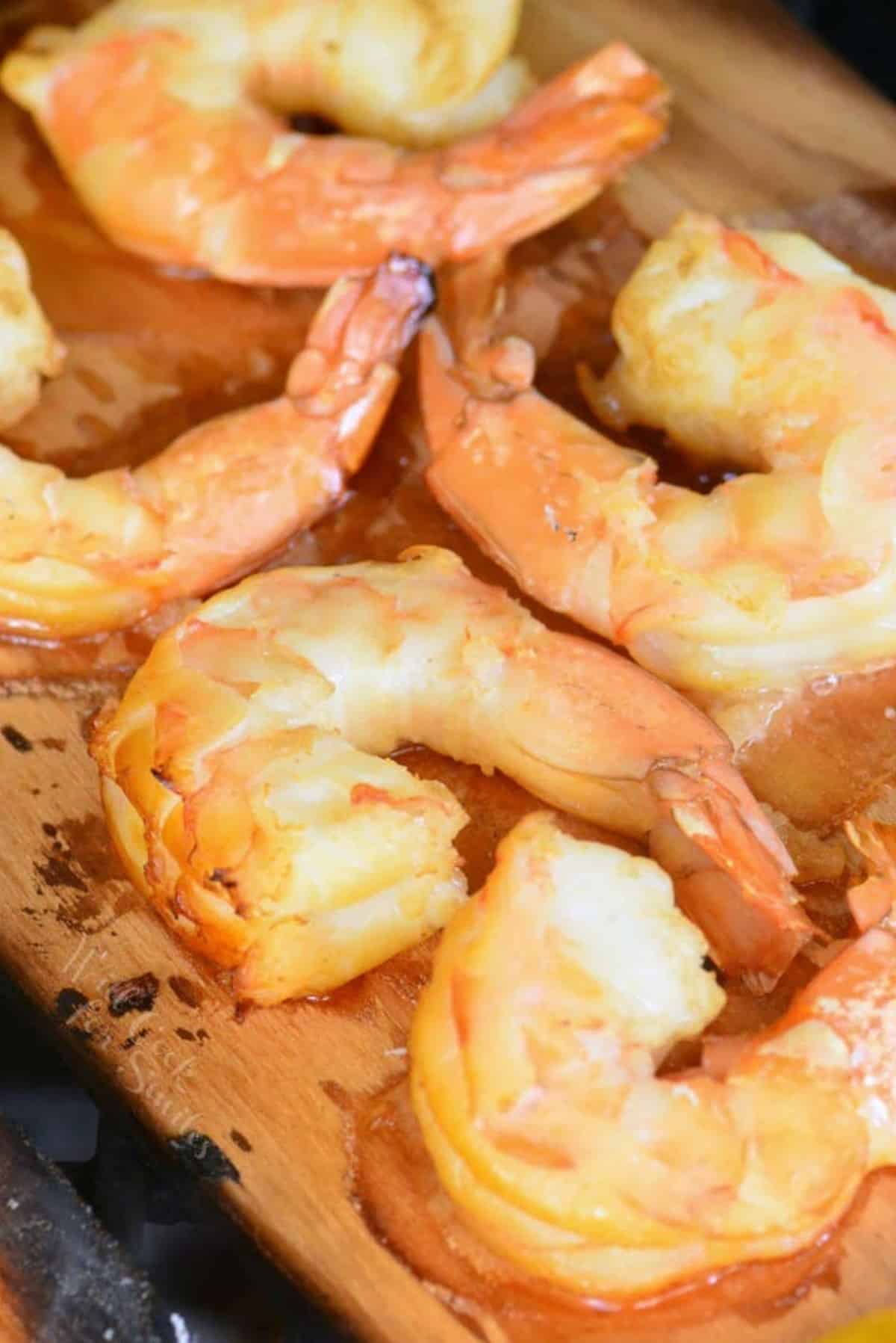 Cooked shrimp are presented on a cedar plank. 