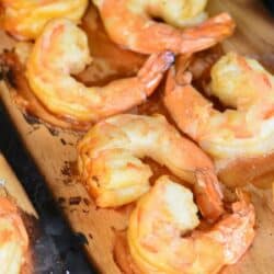 wooden plank with several shrimp on top and lemon on the grill.