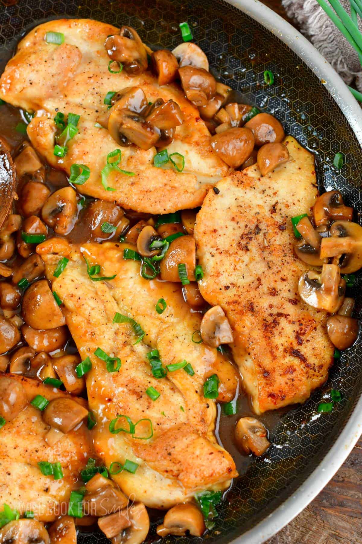 three chicken cutlets surrounded by mushrooms and sauce in the cooking pan.
