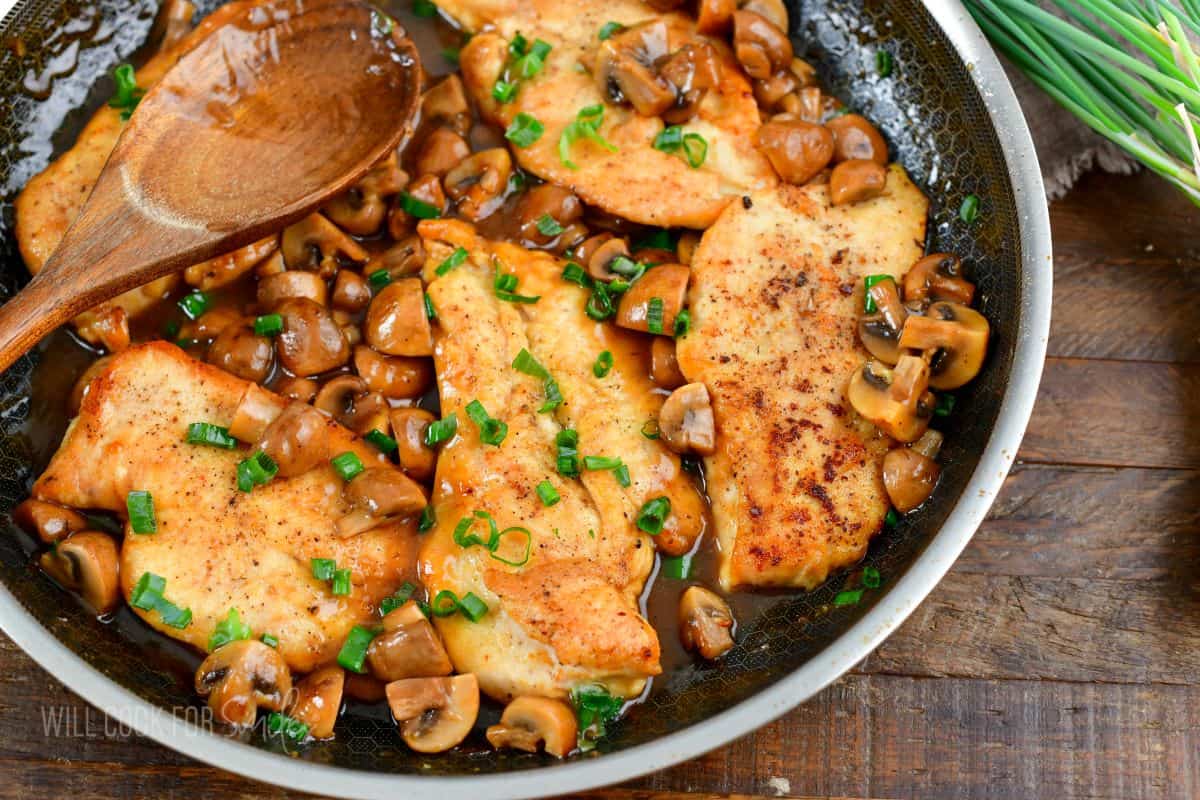 several chicken cutlets in the cooking pan with mushrooms, and topped with chives.