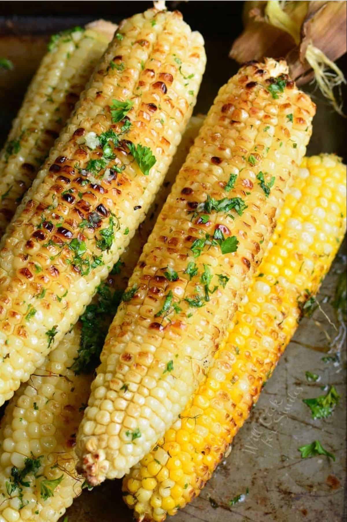 several cobs of grilled corn are placed in a small pile on a tray.