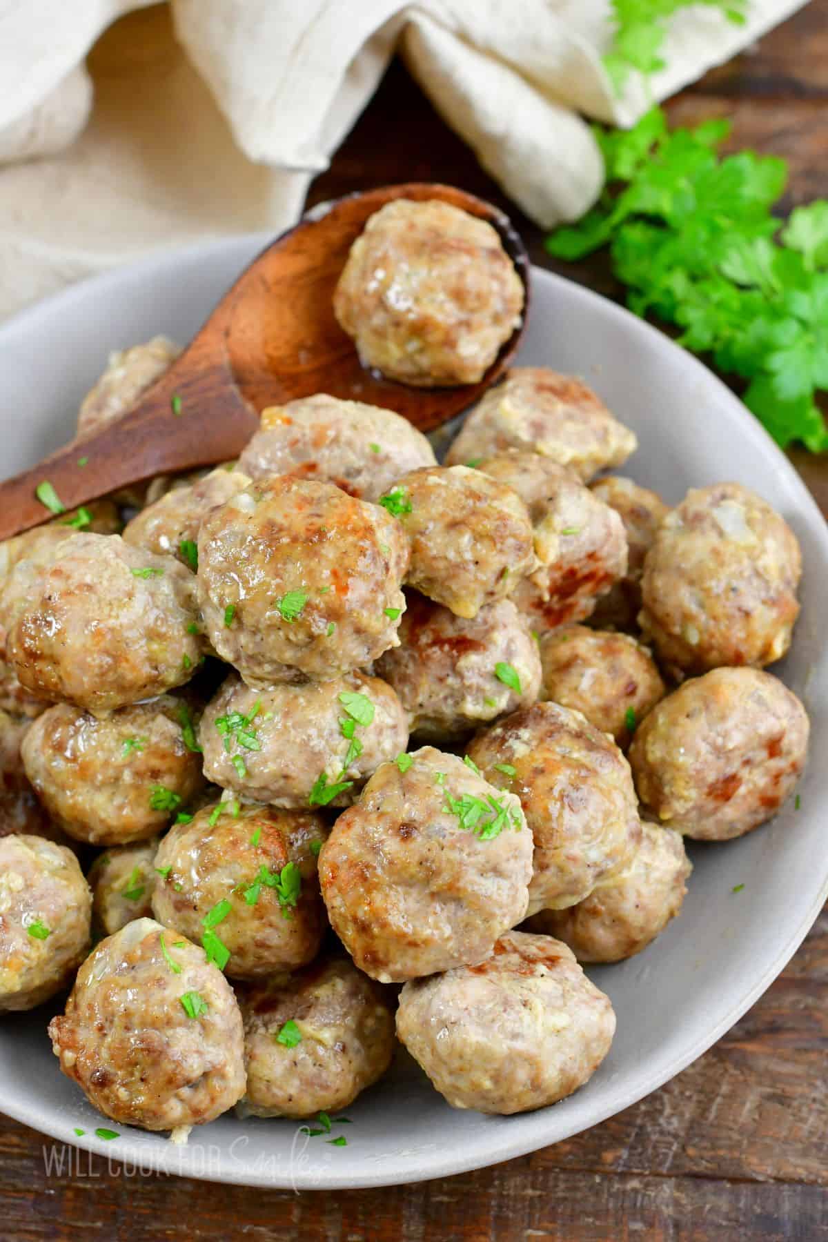 a grey bowl filled with baked basic meatballs and a wooden spoon with one meatball.