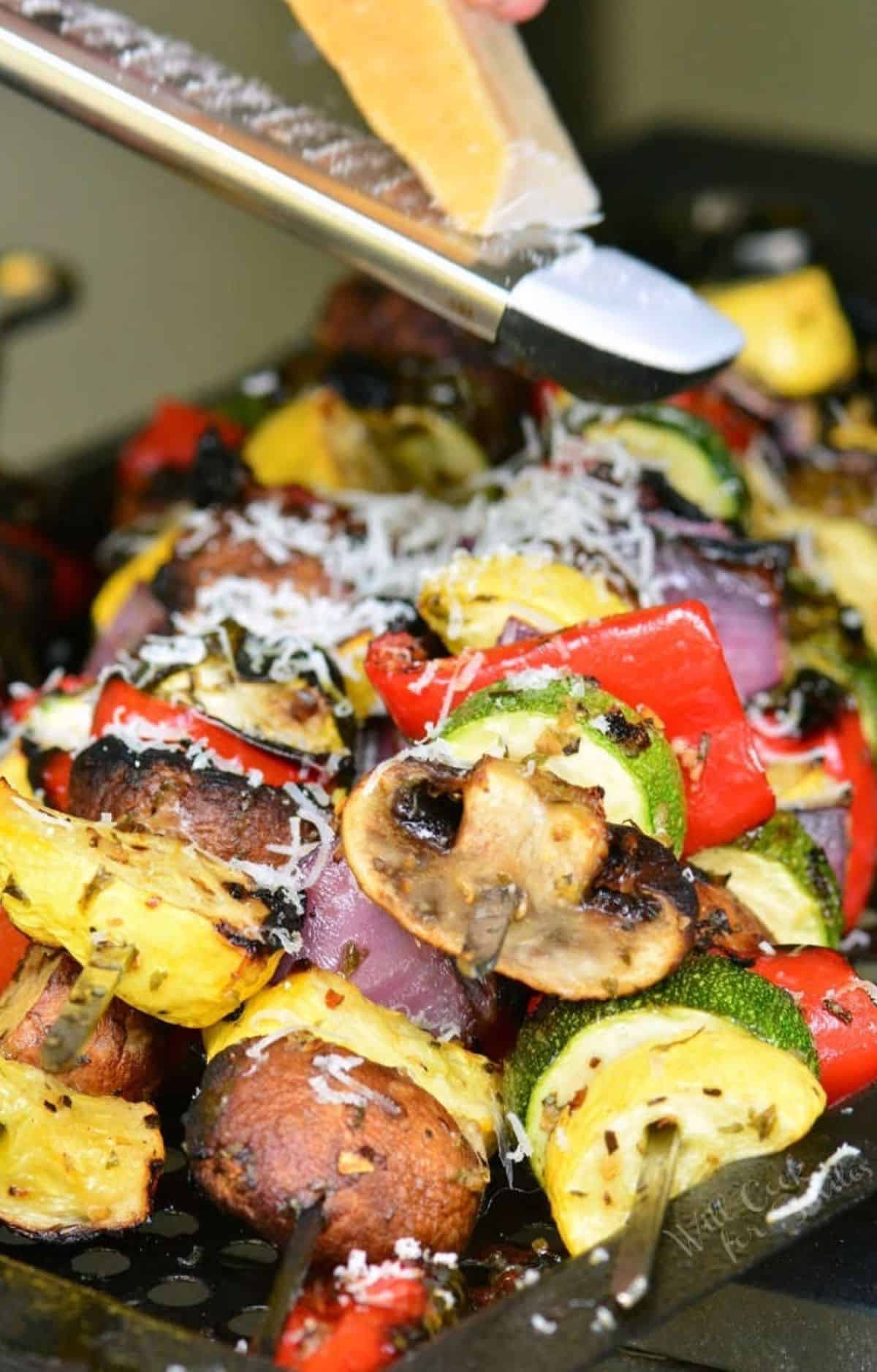 Parmesan cheese is being grated over vegetable skewers.