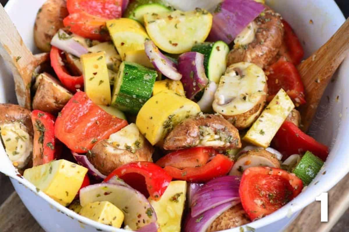 Chopped vegetables are tossed with marinade in a white bowl. 