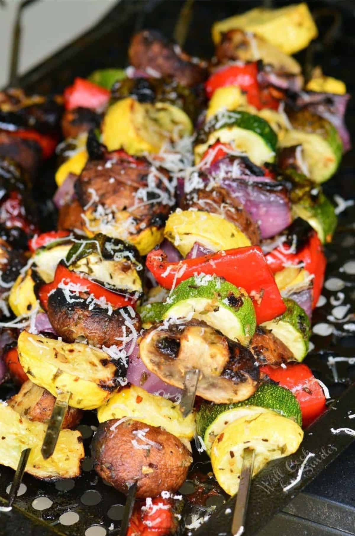 A stack of cheesy Italian vegetable skewers are placed on a black surface. 