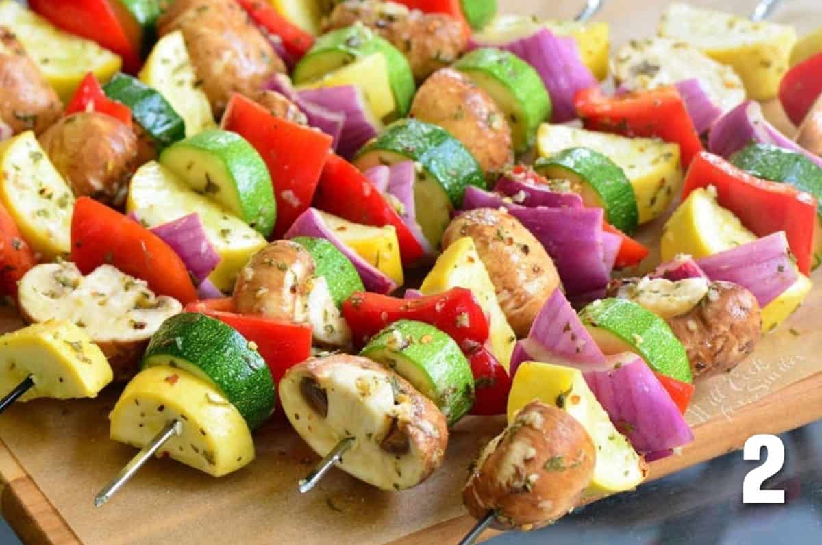 Marinated vegetables are all lined up on metal skewers. 