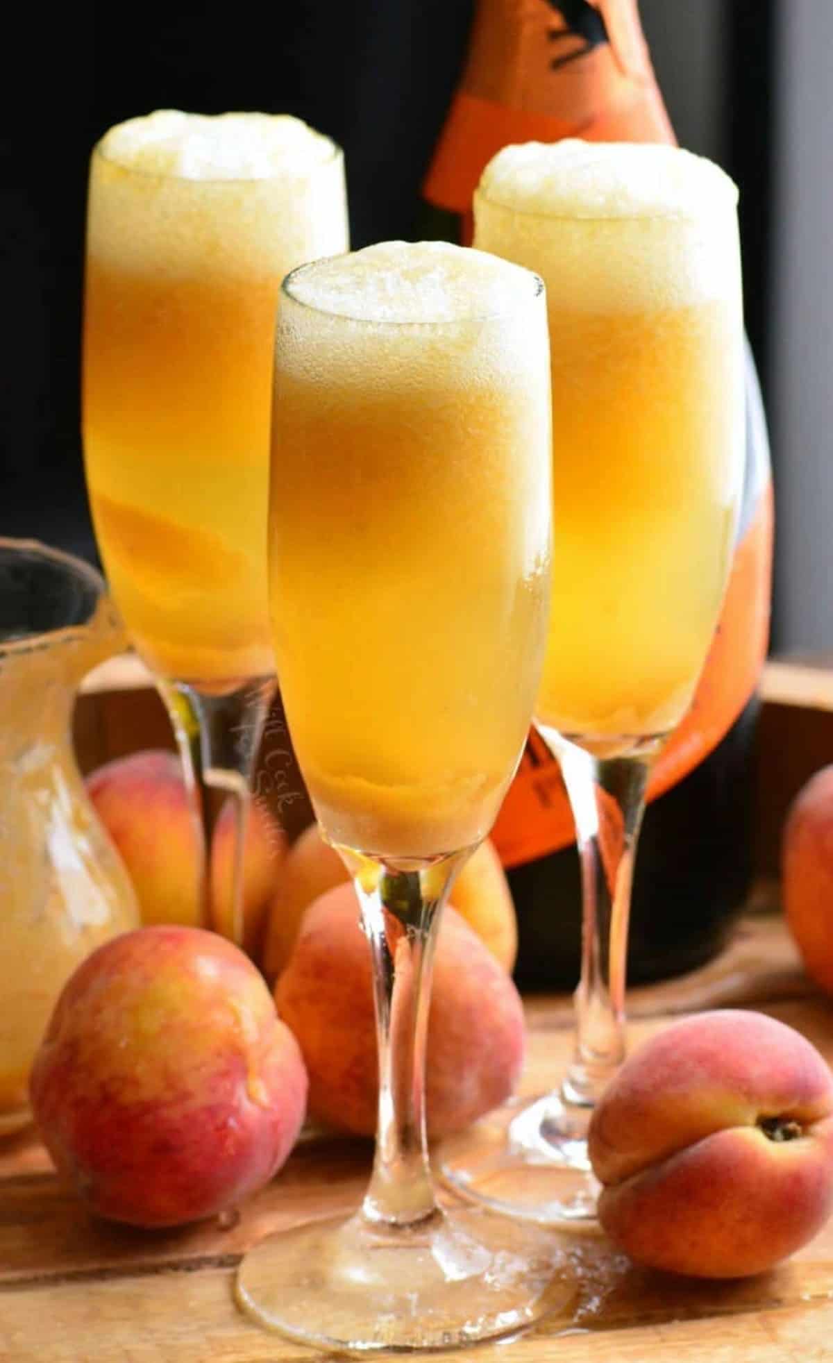 three tall champagne glasses filled with orange peach cocktail and bottle of prosecco. 