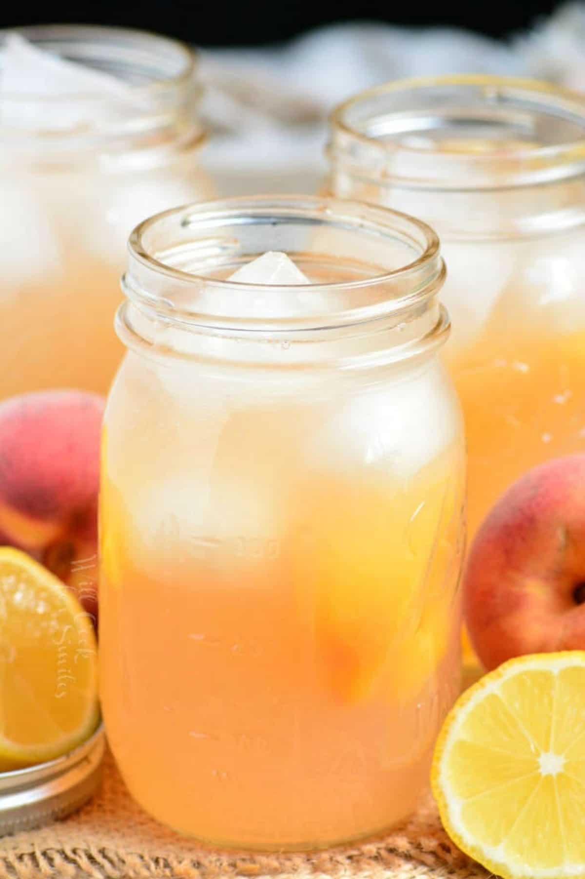 peach lemonade with ice in a mason jar with more on the background.
