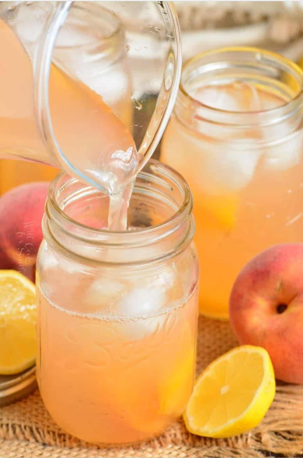 pouring peach lemonade into the mason jaw from a glass jar.