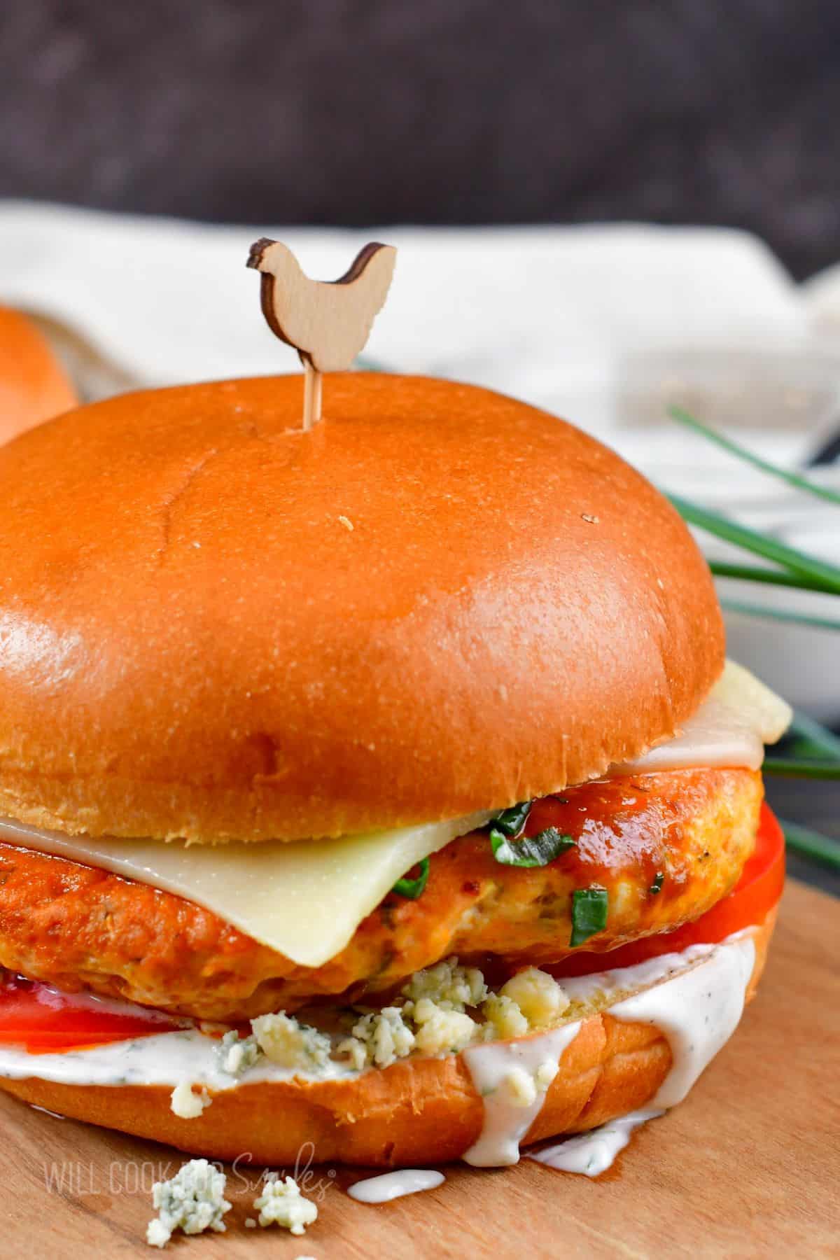 A single buffalo chicken burger is presented on a wooden surface. 