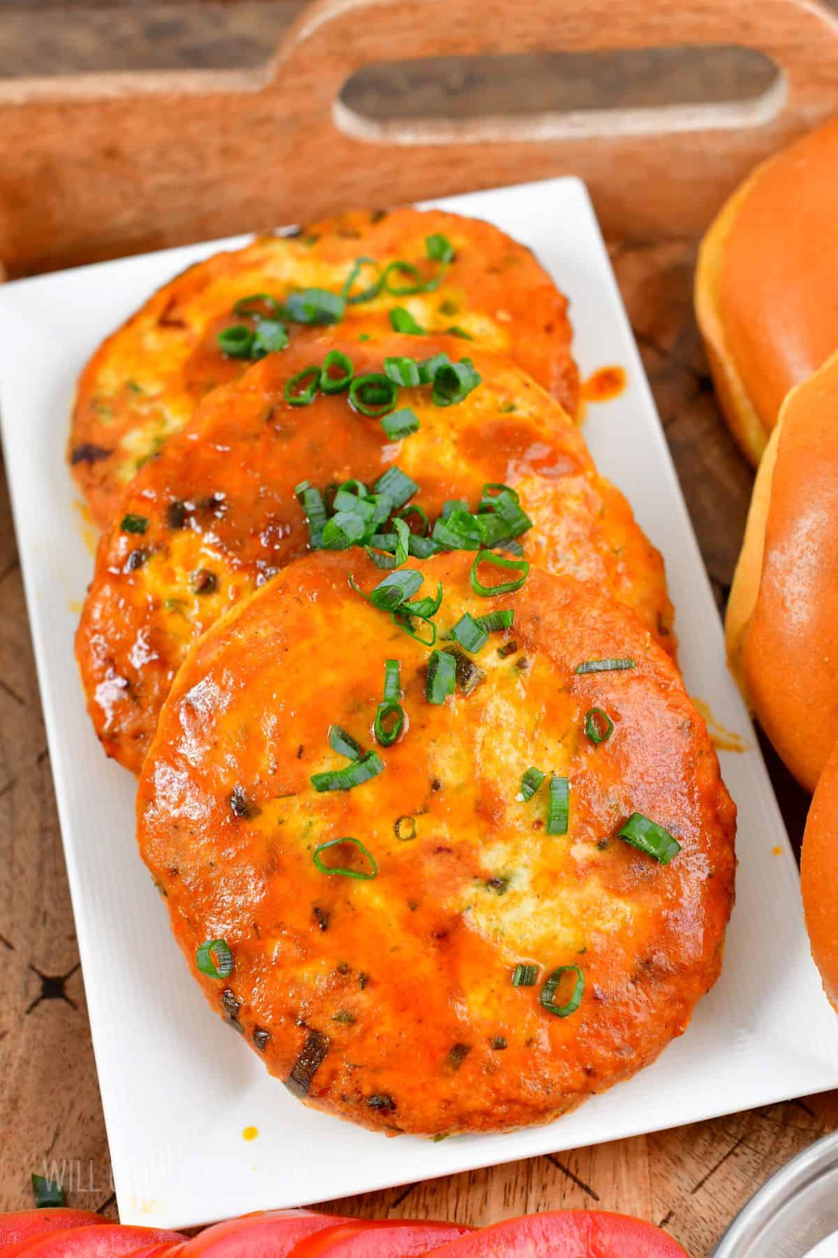 Several cooked buffalo chicken patties are garnished with chopped green onions. 