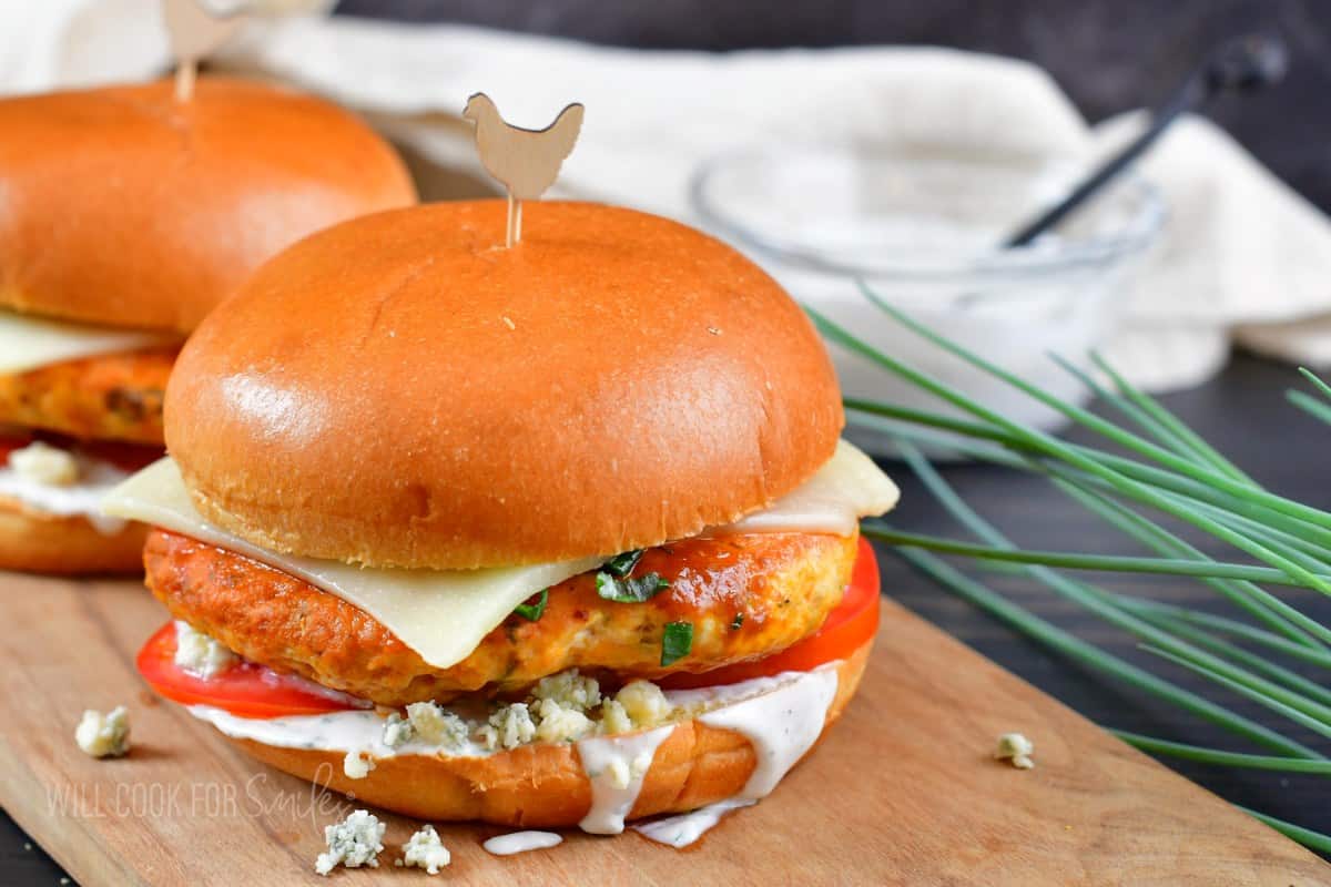 two buffalo chicken burgers on the cutting board, one in front and one behind.