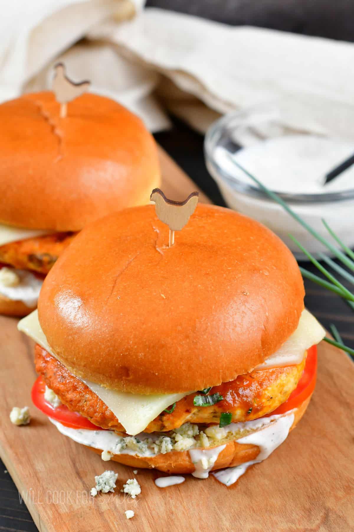 Two buffalo chicken burgers are placed next to each other on a serving board. 