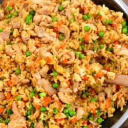 chicken fried rice in a cooking pan with some scooped on a wooden spoon.