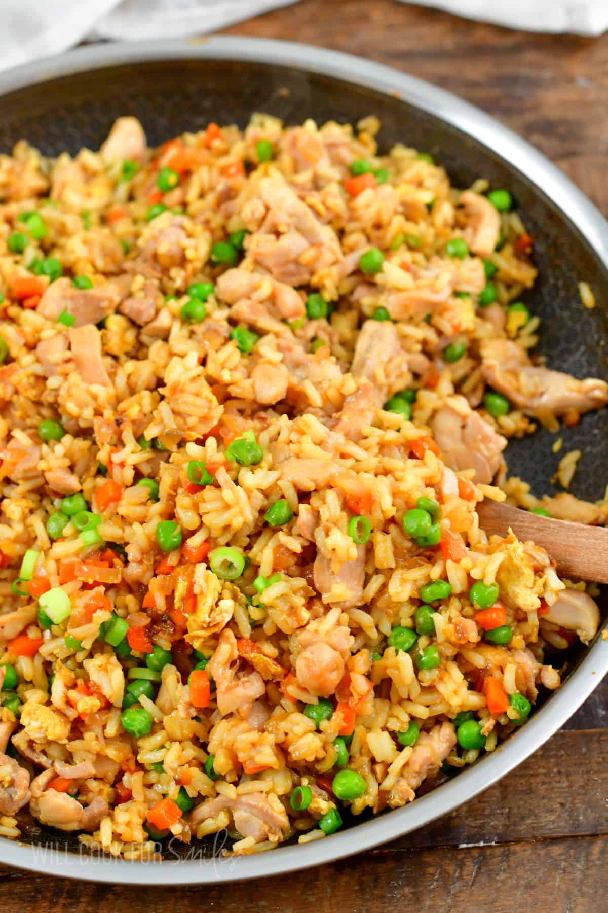 starting to scoop out some chicken fried rice from a pan with wooden spoon.