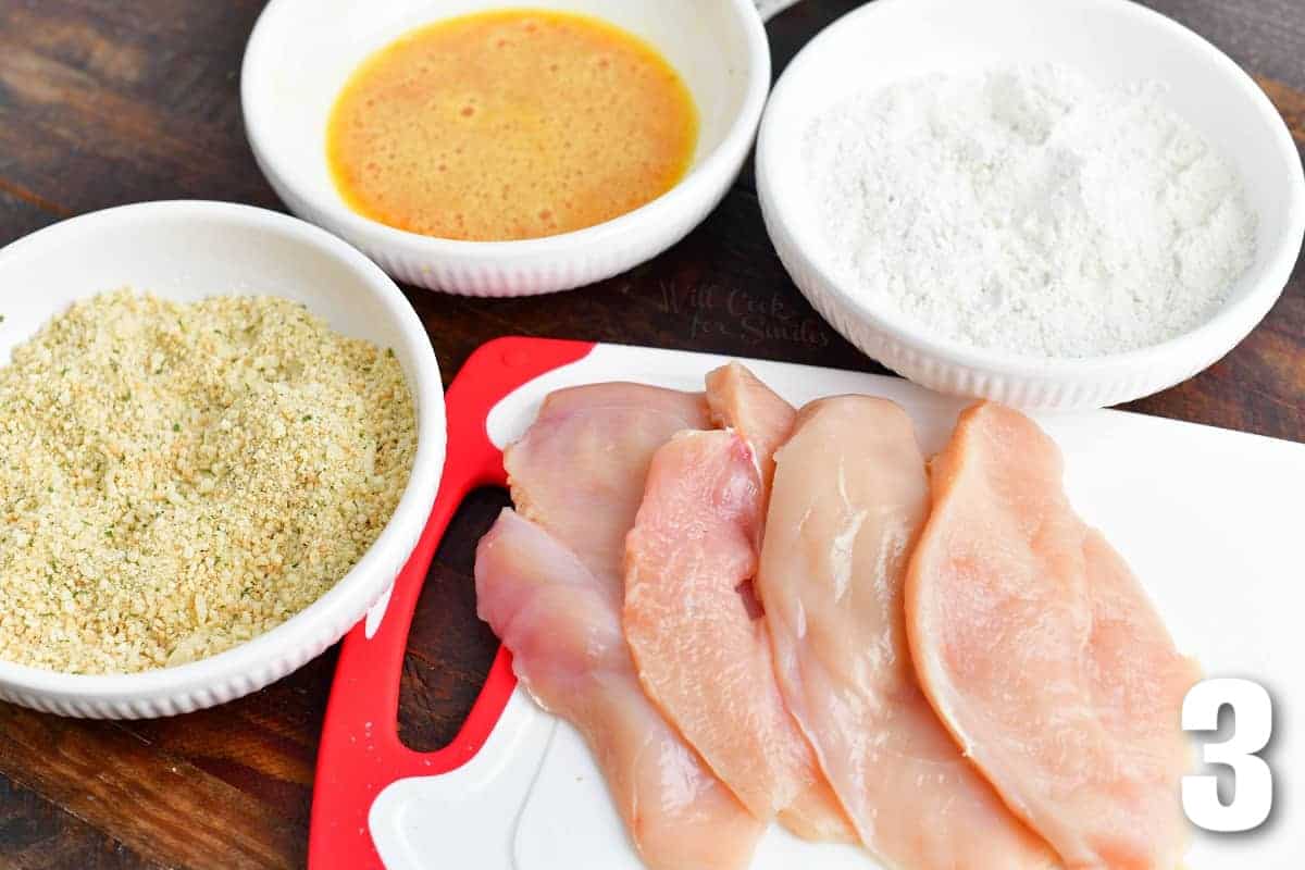 chicken breast cutlets and three bowls of flour, egg, and bread crumbs.
