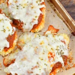 Three pieces of baked chicken parmesan on the baking sheet with melted cheese on top.