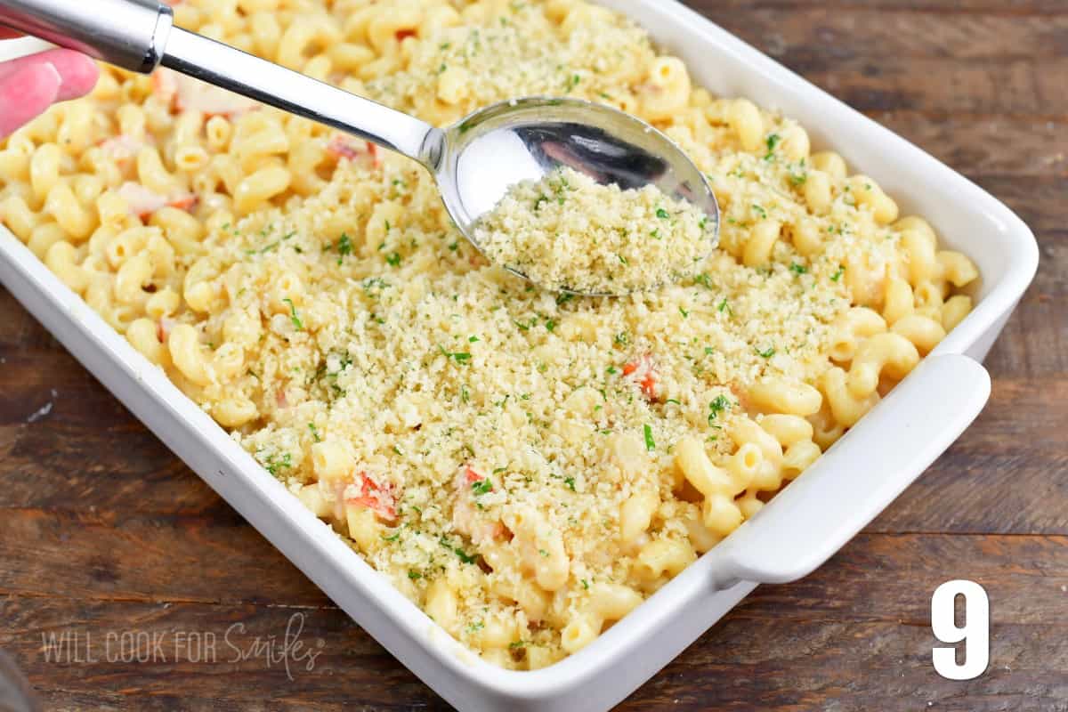 sprinkling panko topping over the mac and cheese with a silver spoon.